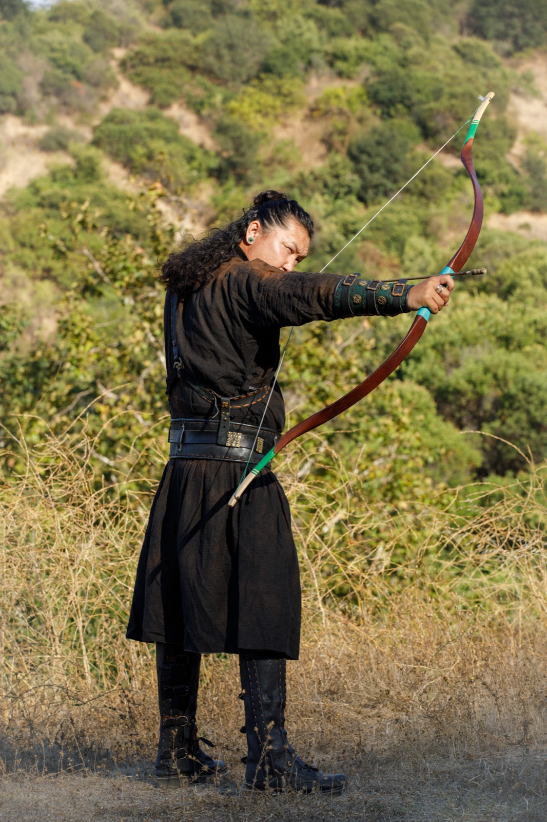 Archer in Mongolian dress drawing a traditional recurve bow