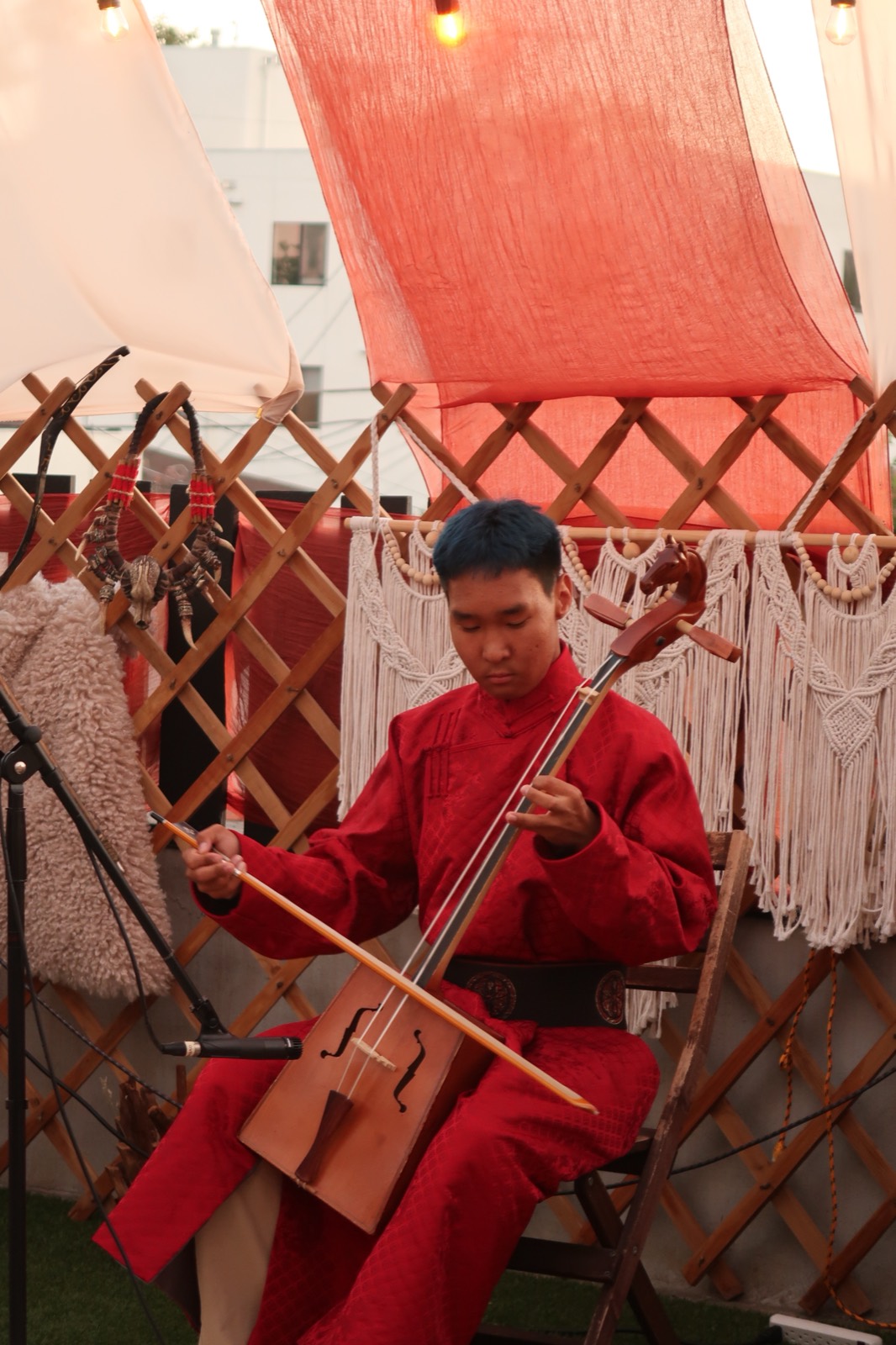 Musician in a red deel playing the morin khuur beside a ger