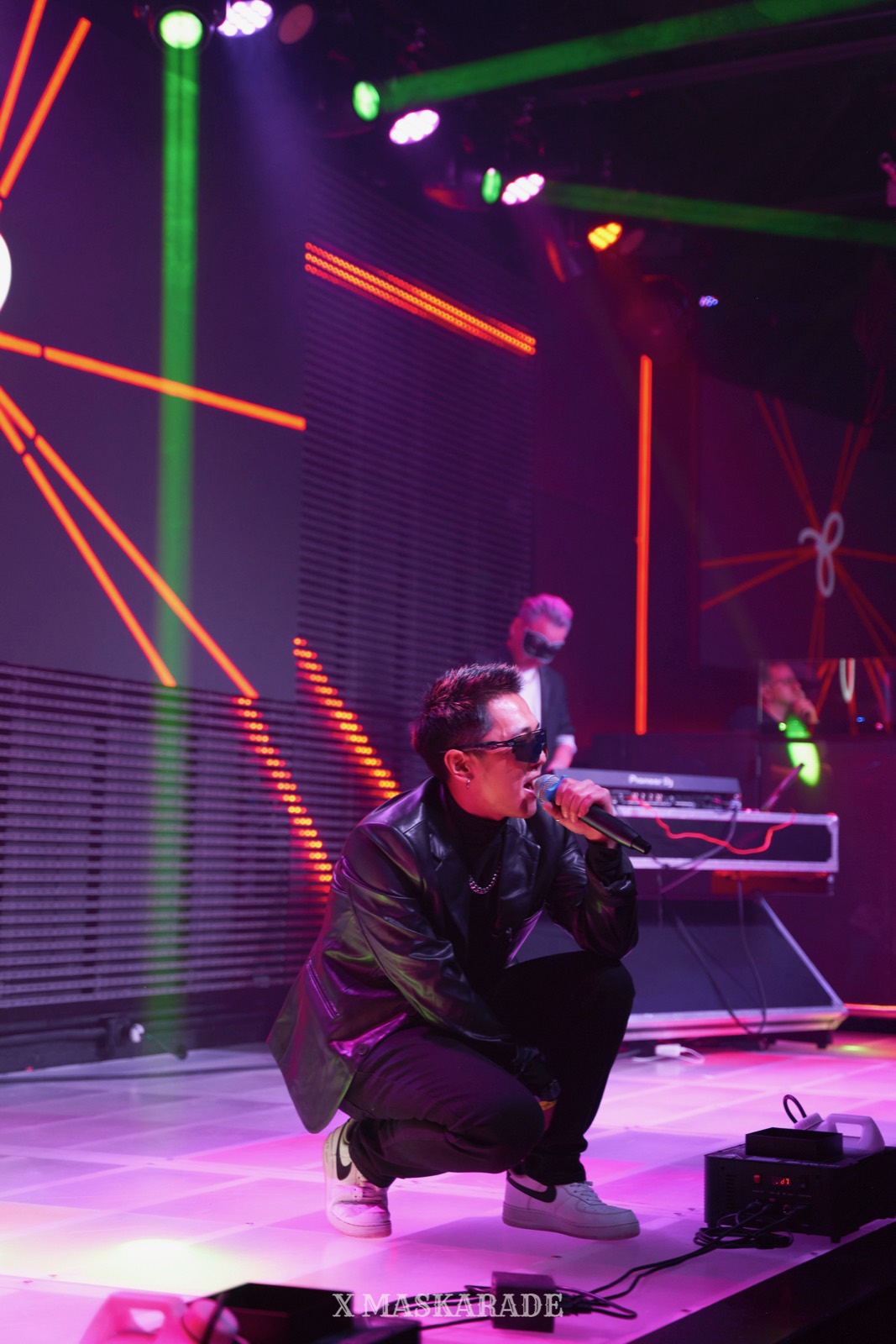 Rapper crouching at the front of a stage under coloured lights