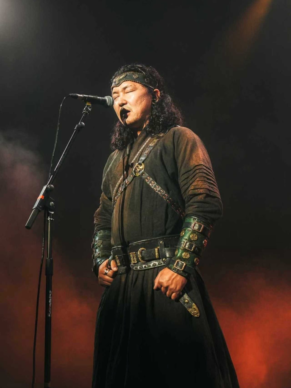 Mongolian singer performing in a traditional deel under stage light